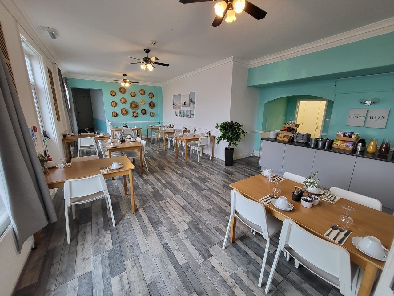 A dining area with multiple tables and chairs, a kitchen area with a counter and appliances, and a ceiling fan.