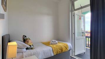 Una habitación de hotel con una cama, una mesita de noche con lámpara, un armario pequeño y un ventanal corredero al exterior.