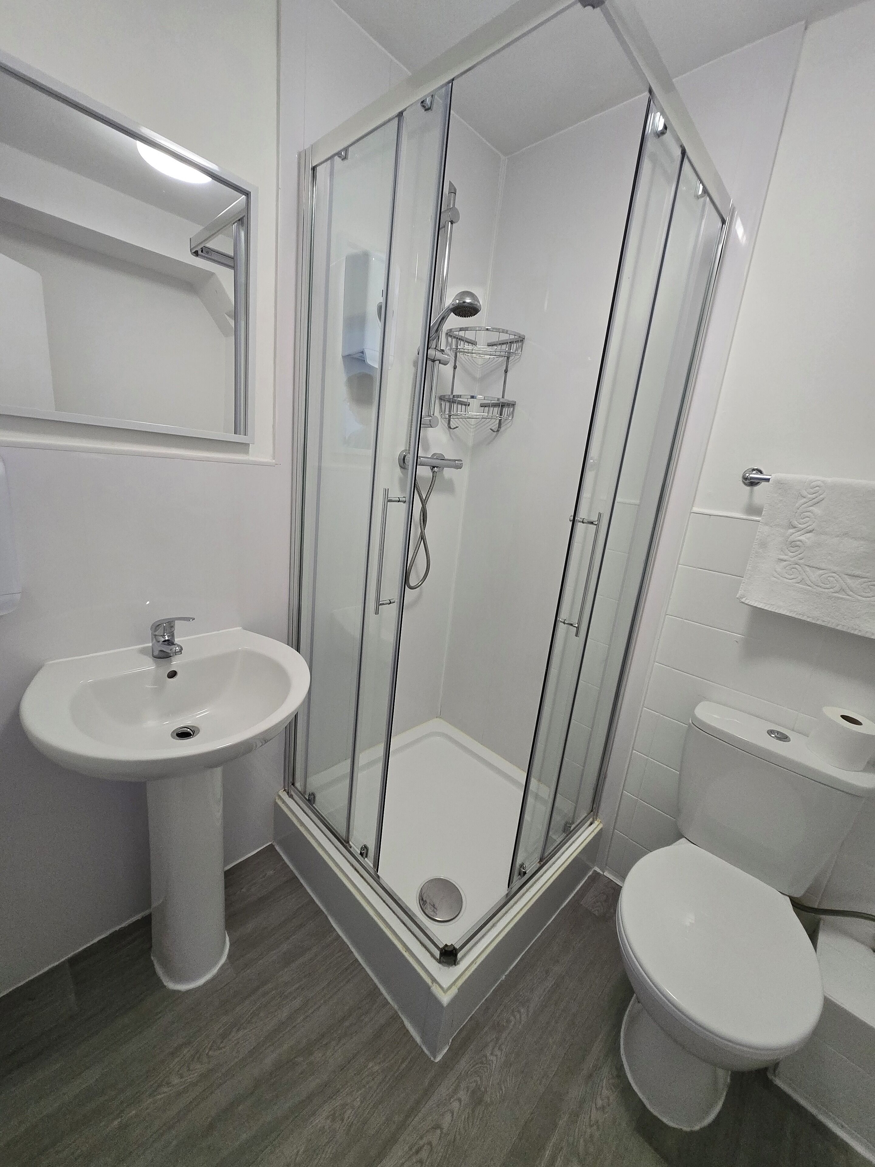 A modern bathroom with a glass-enclosed shower, a pedestal sink, and a toilet.