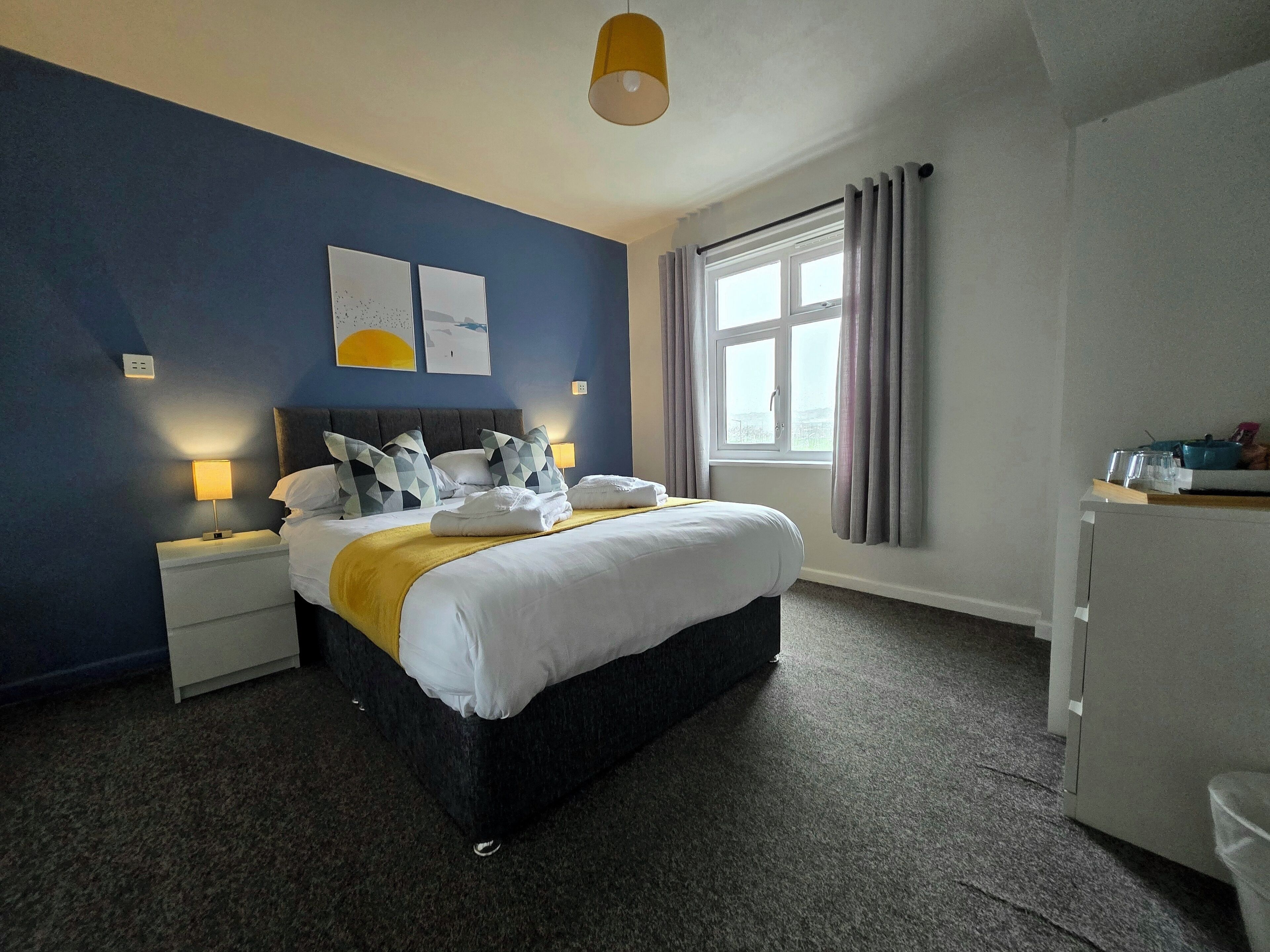 A hotel room with a bed, bedside lamps, a window with curtains, and a view of the outside.