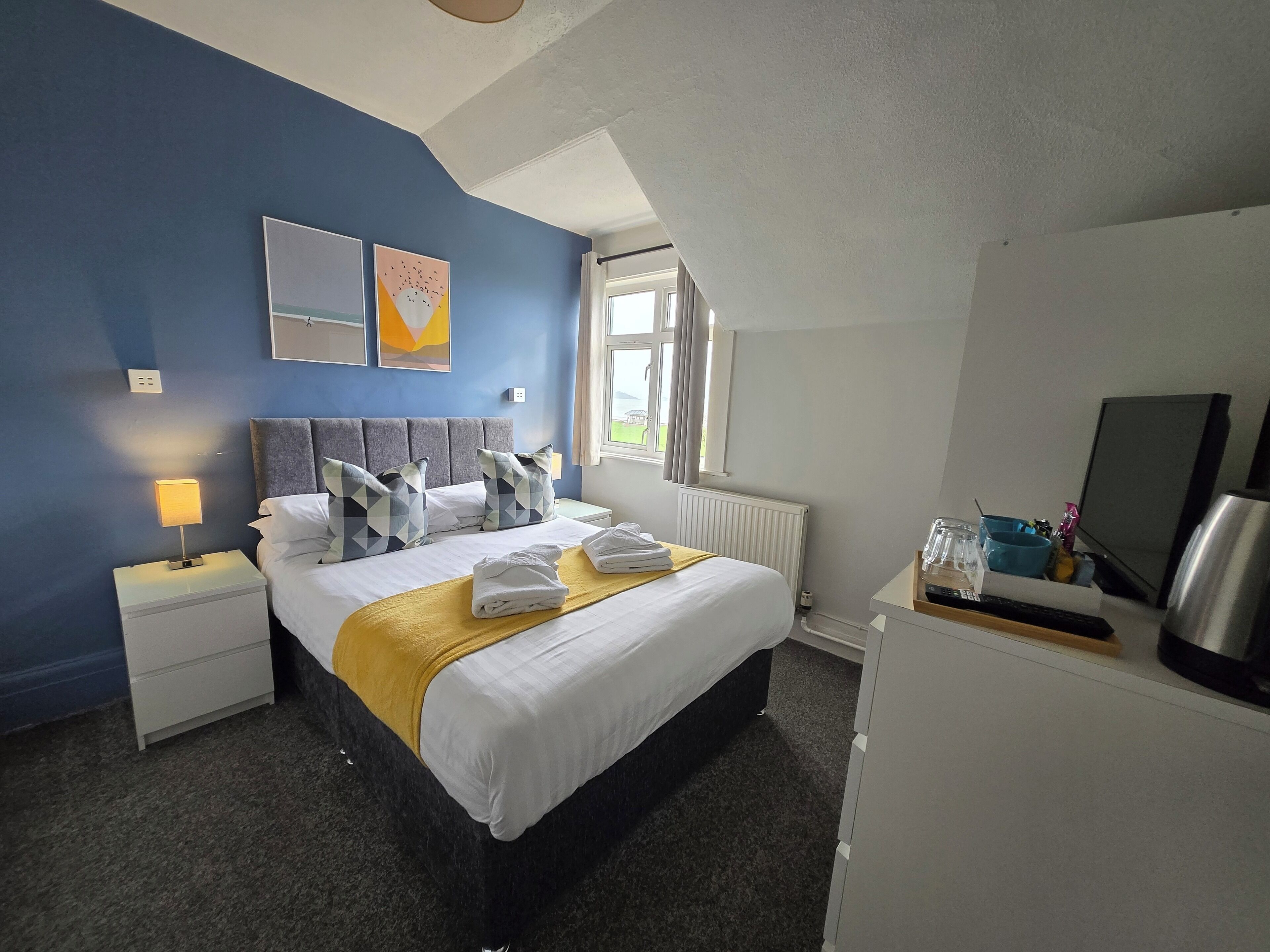 A hotel room with a bed, a nightstand, a desk, a radiator, and a window.