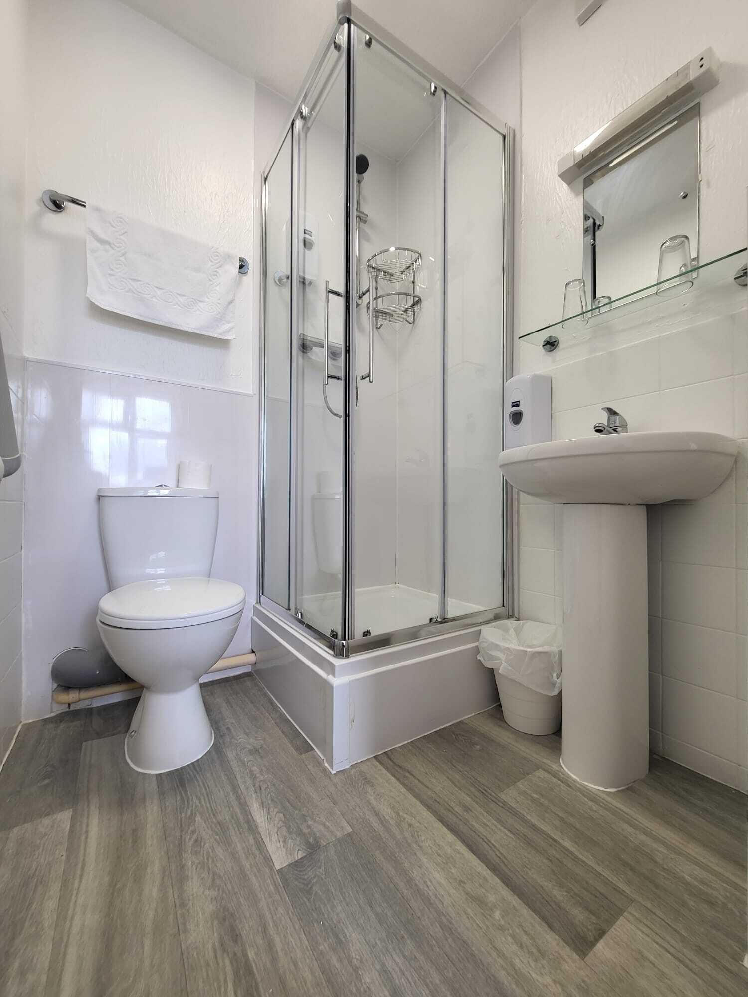 Un baño moderno con ducha de vidrio, inodoro blanco y lavamanos con espejo.