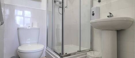 Un baño moderno con ducha de vidrio, inodoro blanco y lavamanos con espejo.