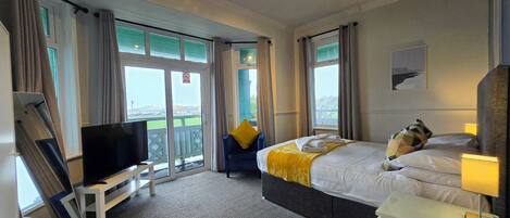 A hotel room with a bed, a TV, a desk, and a balcony with a view of the city.