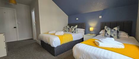 Une chambre d’hôtel avec deux lits, chacun recouvert d’une couverture jaune et de draps blancs, un tapis gris et une armoire blanche.