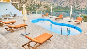 A pool area with lounge chairs and umbrellas, surrounded by a mountainous landscape. - Best Family Friendly Villa Near Lake Kournas (Apokoronas)