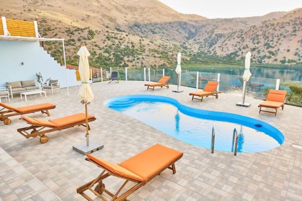 Un espace piscine doté de chaises longues et de parasols, entouré d’un paysage montagneux.