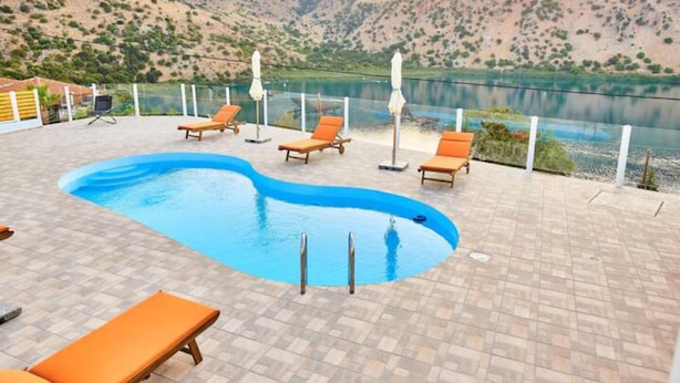 A swimming pool with lounge chairs and umbrellas, surrounded by a mountainous landscape. - Best Family Friendly Villa Near Lake Kournas (Apokoronas)