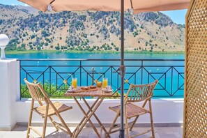 Une table avec deux chaises et un parasol, donnant sur un lac avec des montagnes en arrière-plan.