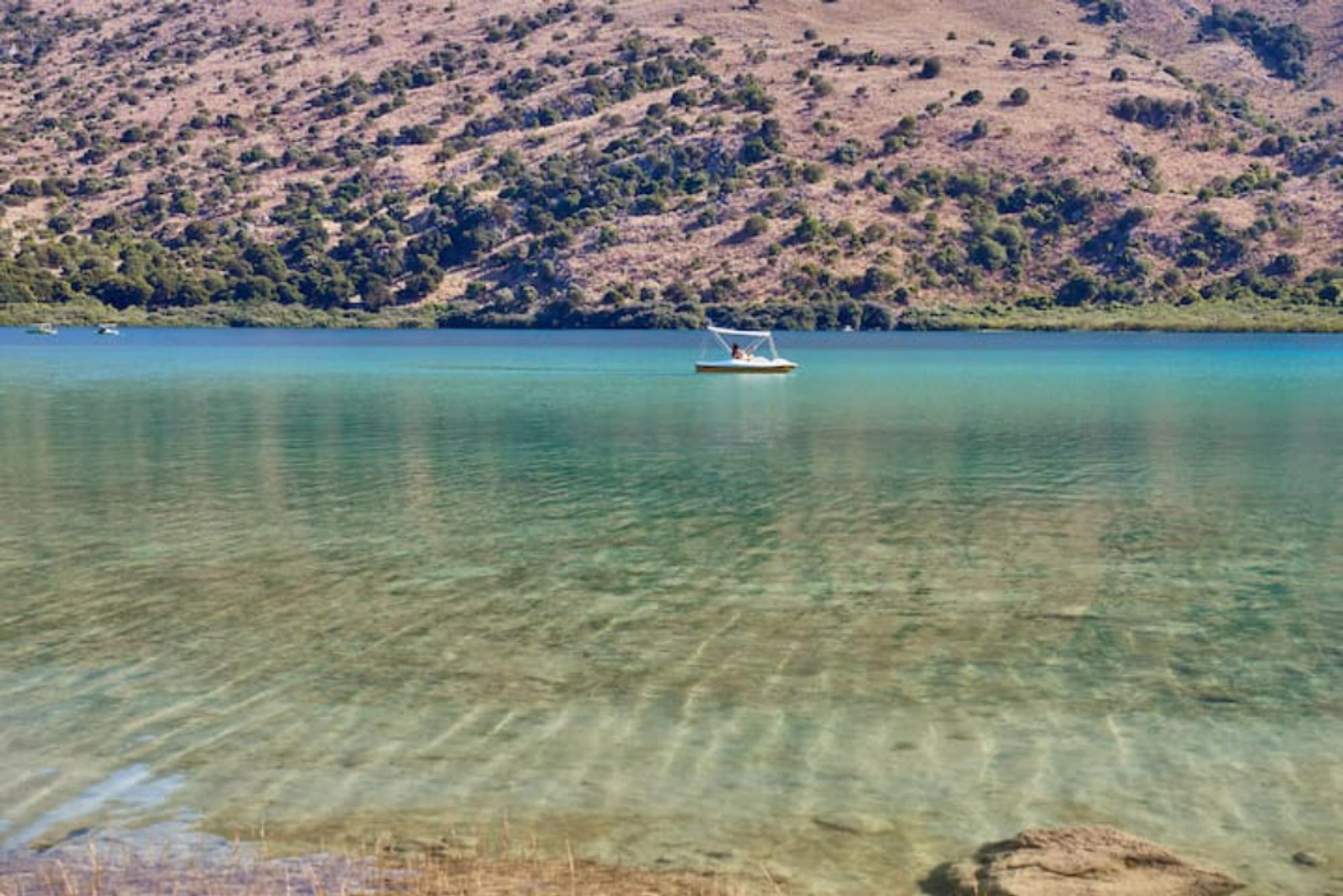Um barco em um lago calmo com paisagem montanhosa ao fundo.