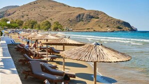 A beach with sun loungers and thatched umbrellas, a sandy shore, and a hill in the background. - Stunning Lake Kournas Retreat 2 New Private Pool (Apokoronas)