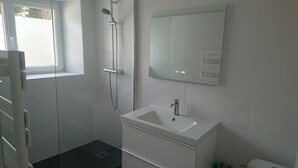 Un bagno moderno con doccia, lavandino e specchio.