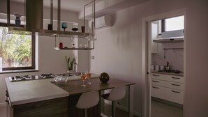 A modern kitchen with a central island, bar stools, and a window overlooking greenery. - Alcantara Home view (Gravà - Castiglione di Sicilia)