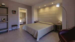 A modern bedroom with a large bed, bedside tables, a small bench, a wardrobe, and a bathroom visible through an open door. - Alcantara Home view (Gravà - Castiglione di Sicilia)