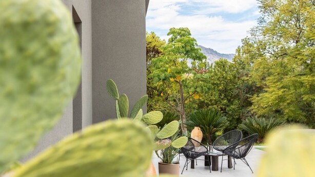An outdoor patio with a table and chairs, surrounded by various plants and trees. - Alcantara Home view (Gravà - Castiglione di Sicilia)