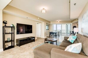 Un salón amplio con una televisión de pantalla plana, un mueble de entretenimiento oscuro, un sofá marrón y una mesa de centro redonda.
