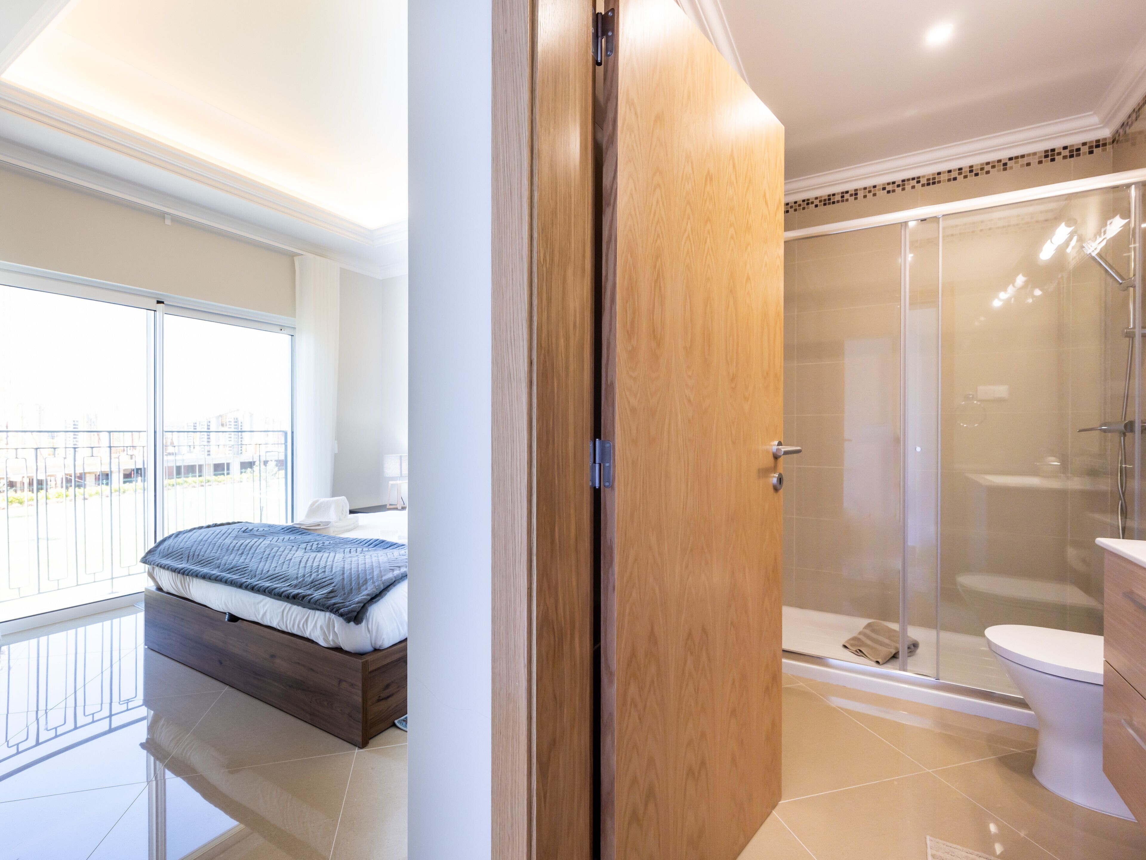 A modern hotel room with a balcony, a wooden wardrobe, a glass shower enclosure, and a separate toilet area.