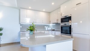 A modern kitchen with white cabinetry, a central island, and built-in appliances. - Casa Malhotra at Boa Vista Golf Resort, Bayview Village (Lagos)
