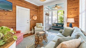 Un salon chaleureux avec un mur en bois, un téléviseur fixé au mur, un canapé confortable, un fauteuil agrémenté d’un coussin coloré et une petite table avec un plateau.