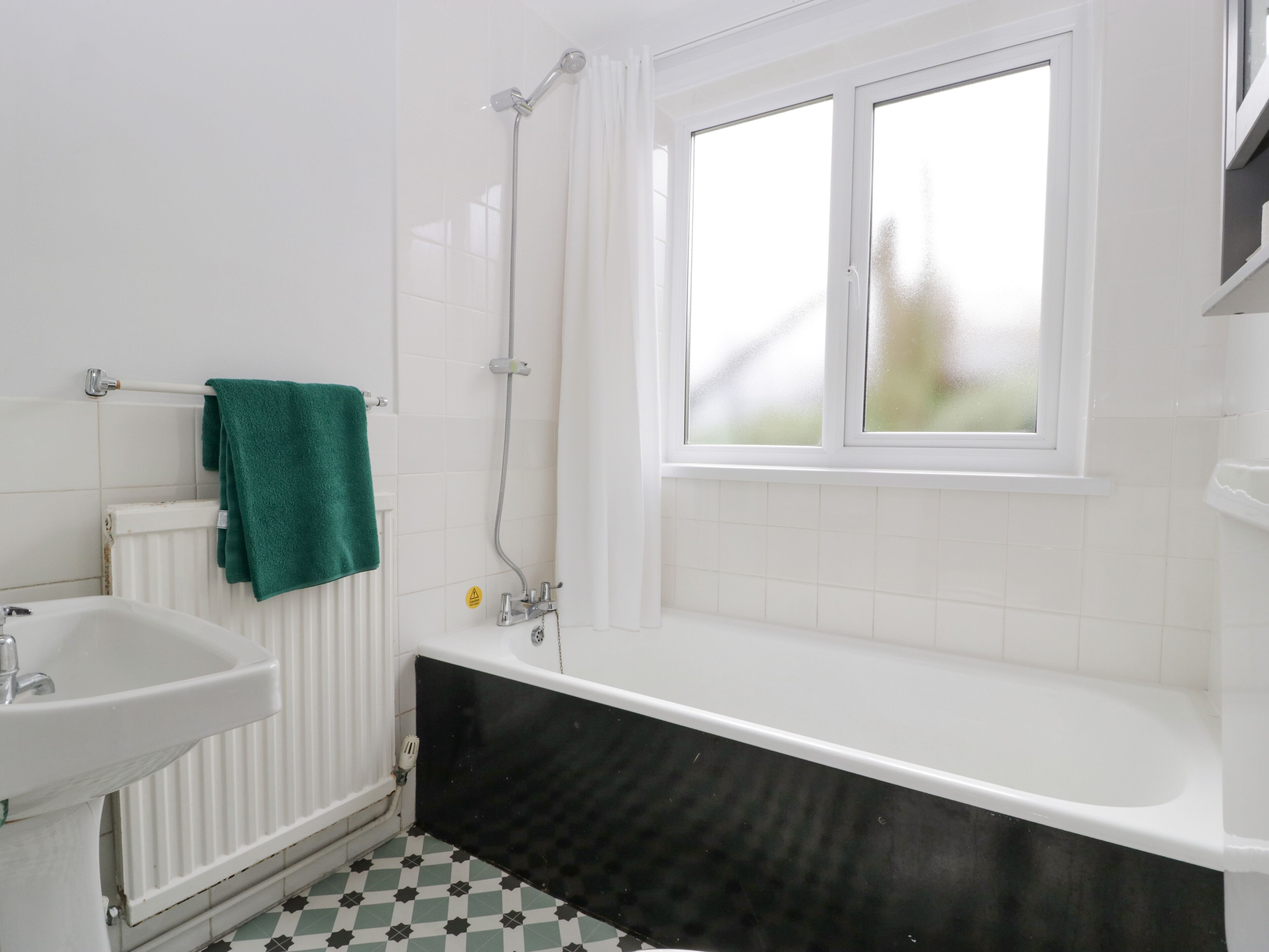 Un baño con una bañera blanca, una ventana, un radiador y un lavabo.