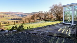 A patio with a stone floor, a glass conservatory, and a view of rolling hills. - Ty Twmp / Tump Cottage (Brecon)