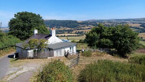 A white house with a grey roof, surrounded by greenery and a clear blue sky. - Ty Twmp / Tump Cottage (Brecon)