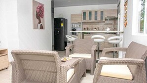 Una cocina moderna con armarios blancos y un refrigerador negro. Hay sillas de mimbre y una pequeña mesa de comedor.