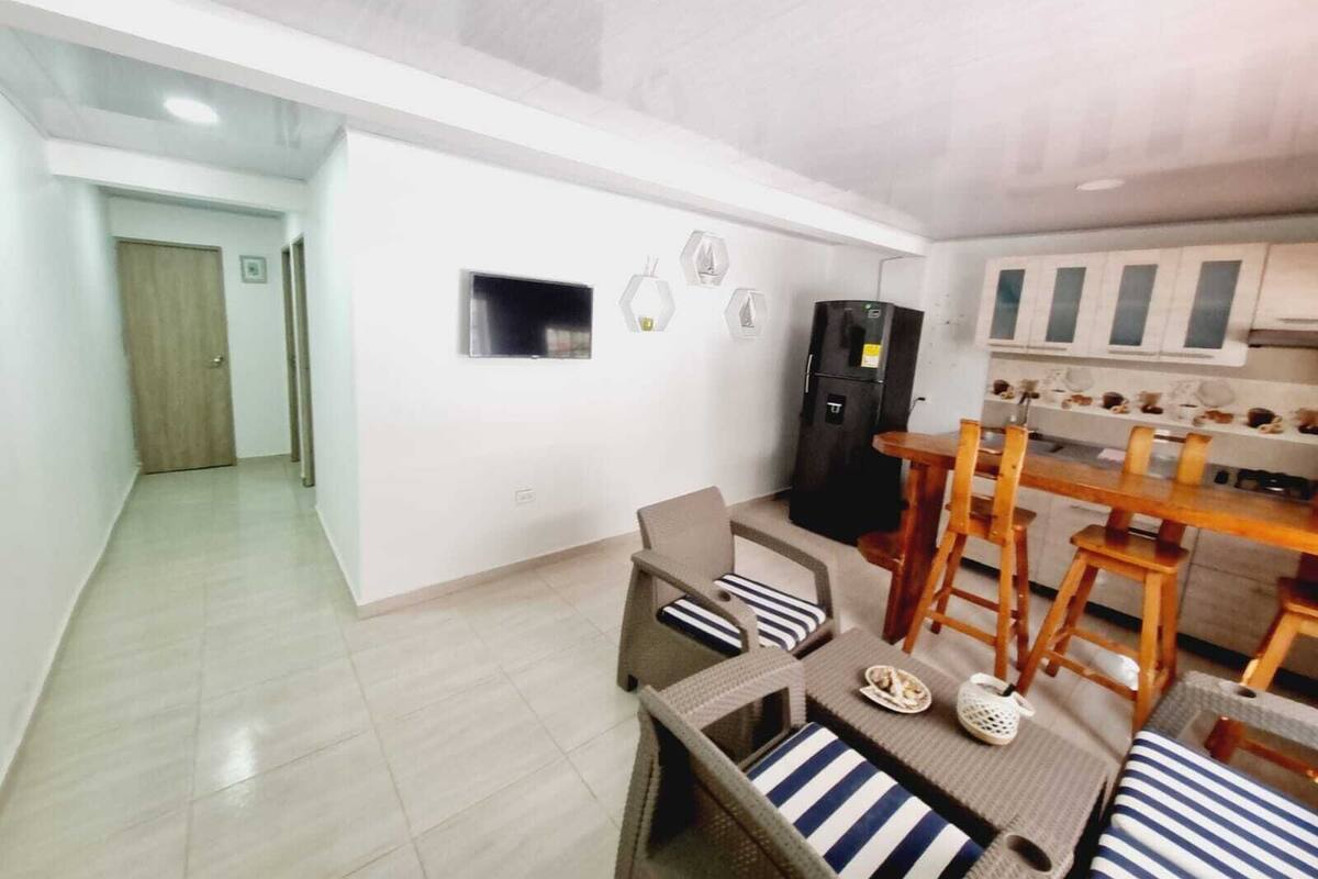 A modern kitchen with white cabinets, a black refrigerator, and a dining area with a wooden table and wicker chairs.