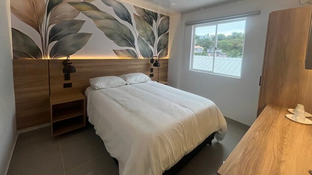 A bedroom with a bed, a nightstand, a wall-mounted lamp, and a window. - Apartamentos Turisticos Altamar (San Andrés)