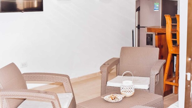 Un comedor con mobiliario de mimbre, una mesa pequeña con un plato de comida y un refrigerador al fondo.