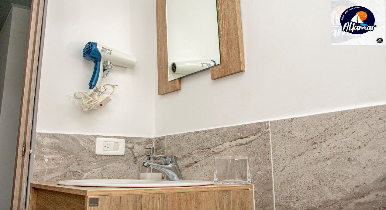 A bathroom with a marble backsplash, a sink, a mirror, a blue hairdryer, and a glass.