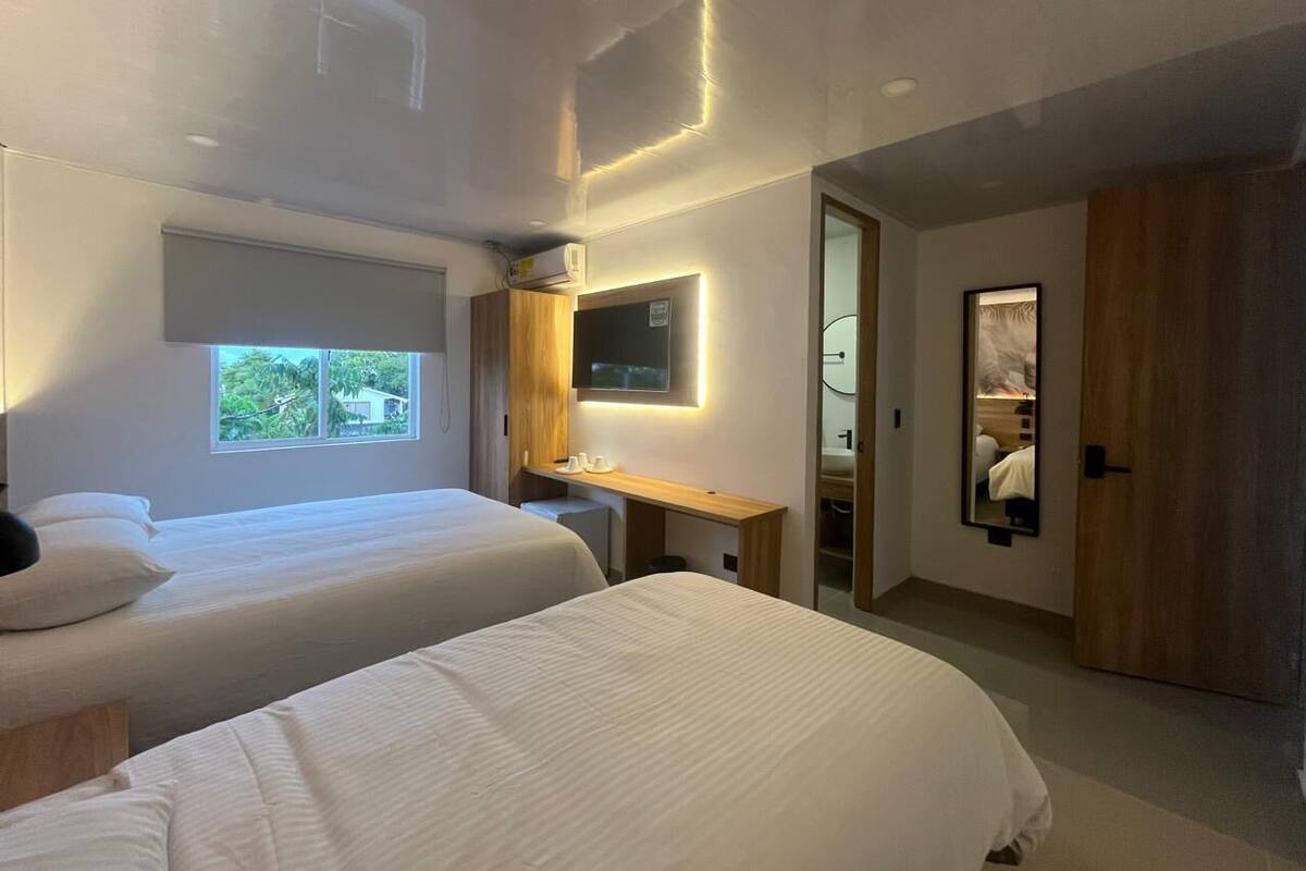 A modern hotel room with two beds, a desk, a TV, and a large mirror.