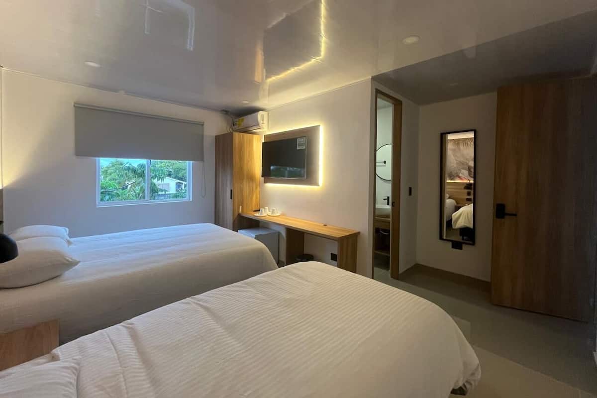 Una habitación de hotel moderna con dos camas, un escritorio, un televisor y un espejo grande.