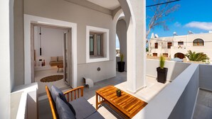 A balcony with a wooden table and chairs, a potted plant, and a view of neighboring buildings.