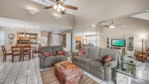 A spacious living room with a large gray sofa, a glass coffee table, and a dining area with wooden chairs and a chandelier. - 3BD Villa Sandestin Resort, Golf Cart Included (Destin)