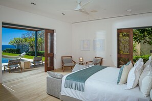 Une chambre avec un grand lit, deux fauteuils, une petite table et une vue sur la mer.