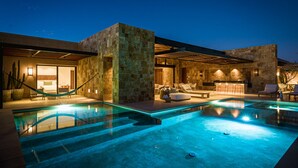 Area piscina moderna all'aperto, con muri in pietra, un'amaca e un angolo bar con posti a sedere.