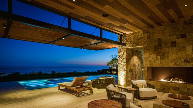Una moderna area relax esterna con piscina, mobili in legno e un muro in pietra.
