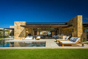 Une maison moderne dotée d’une piscine, d’un espace salon extérieur et d’un patio couvert.
