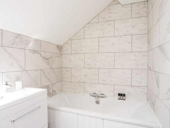 A bathroom with a white bathtub, marble tiles, and a white vanity with drawers.