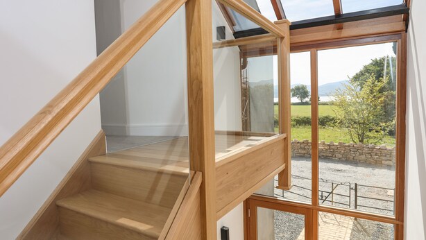 A wooden staircase with glass railings leading to a balcony with a view of a rural landscape.