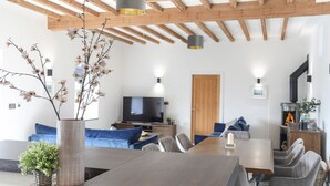 A modern living room with a wooden ceiling, a dining table, sofas, and a TV.