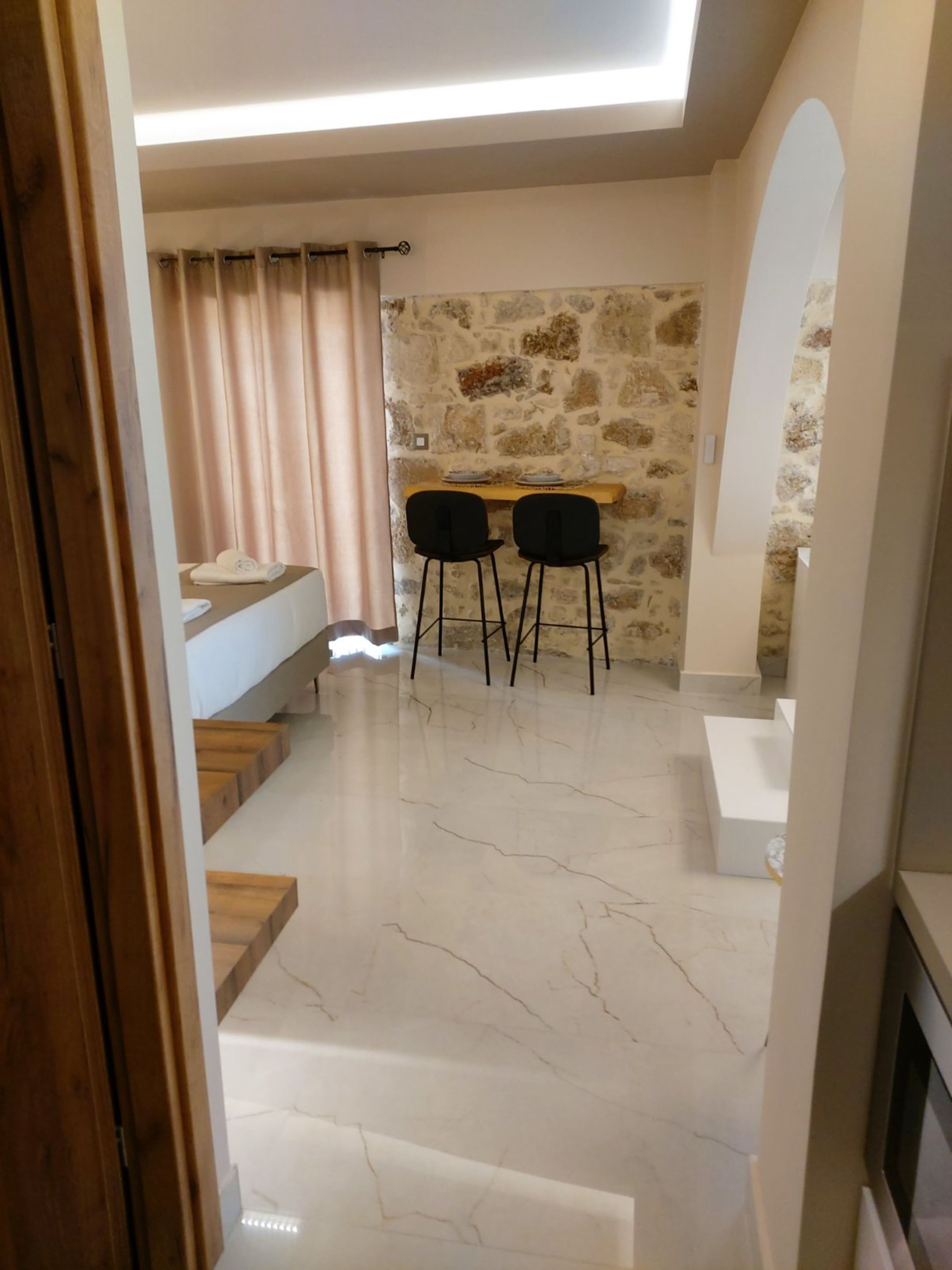 A modern interior with a stone wall, a dining area with two chairs, and a staircase leading to a lower level.