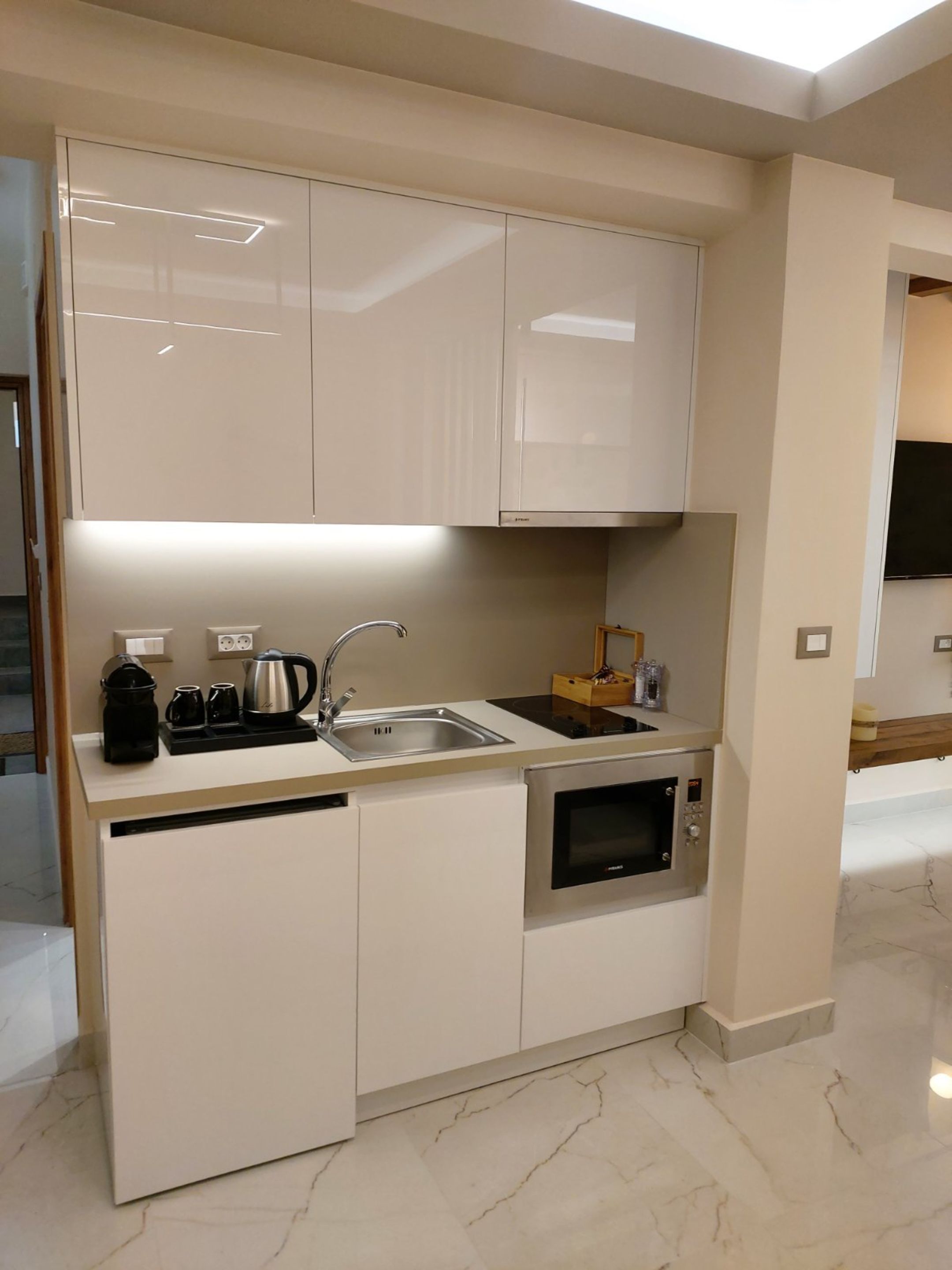 Una cocina moderna con armarios blancos, un lavamanos de acero inoxidable, horno empotrado y cafetera.