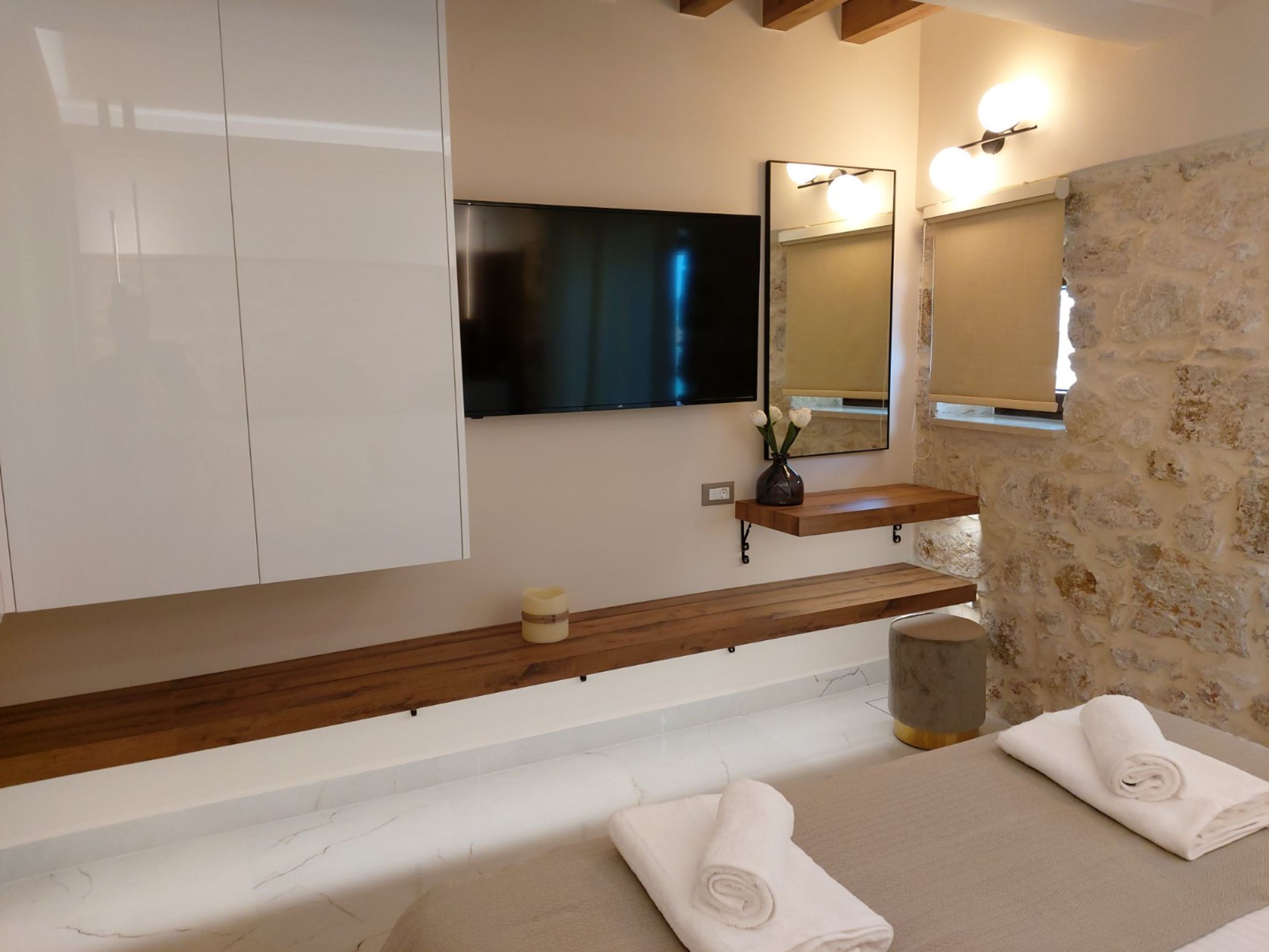 Une salle de bain moderne avec un grand miroir, un téléviseur à écran plat, une étagère en bois et deux serviettes posées sur le sol.