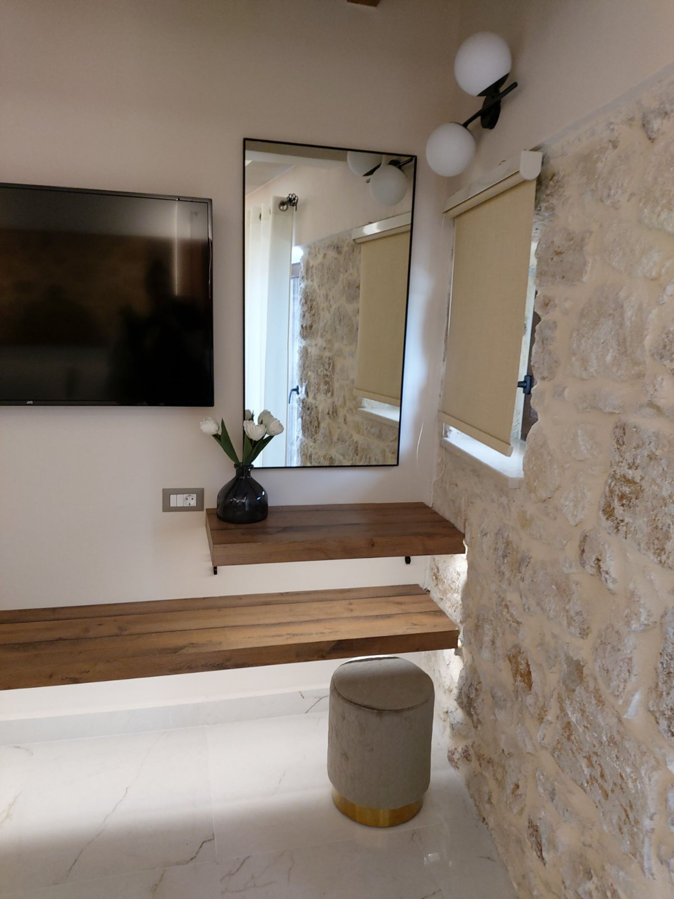 A bathroom with a stone wall, a wooden shelf with a vase, a large mirror, and a toilet.