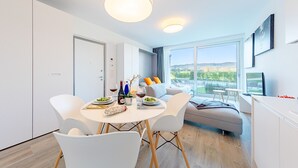 Un espace repas moderne avec une table ronde, des chaises blanches et une vue sur l’extérieur grâce à de grandes fenêtres.