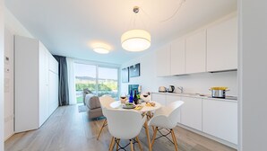 Une cuisine moderne avec des meubles blancs, un coin repas avec des chaises blanches et une grande fenêtre donnant sur un paysage verdoyant.