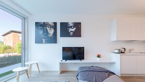 Un salon moderne avec une grande fenêtre, un canapé, un téléviseur et un coin cuisine.