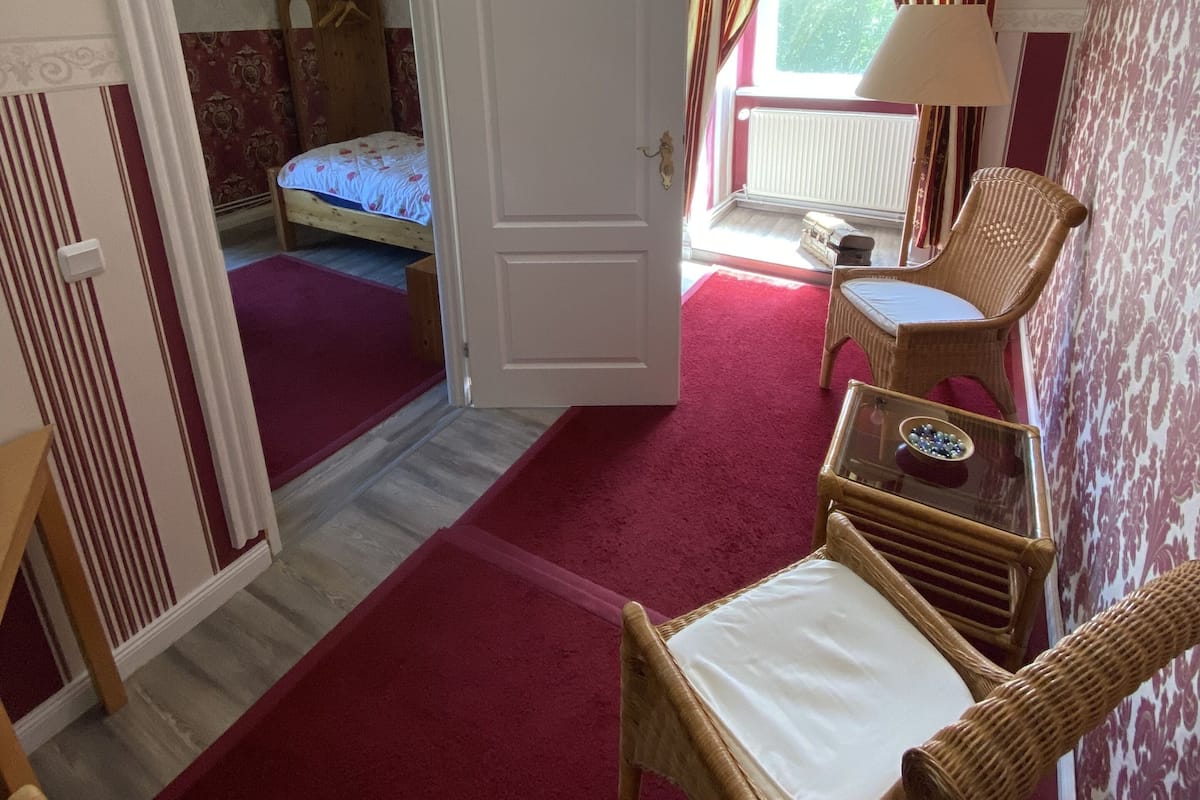 A room with a bed, a chair, a table, and a door leading to another room.